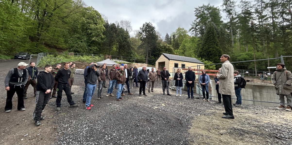 Richtfest Seehundanlage Eine Gruppe von ca. 30 Menschen steht im Halbkreis auf einer Baustelle um einen Mann herum, der eine Rede hält.