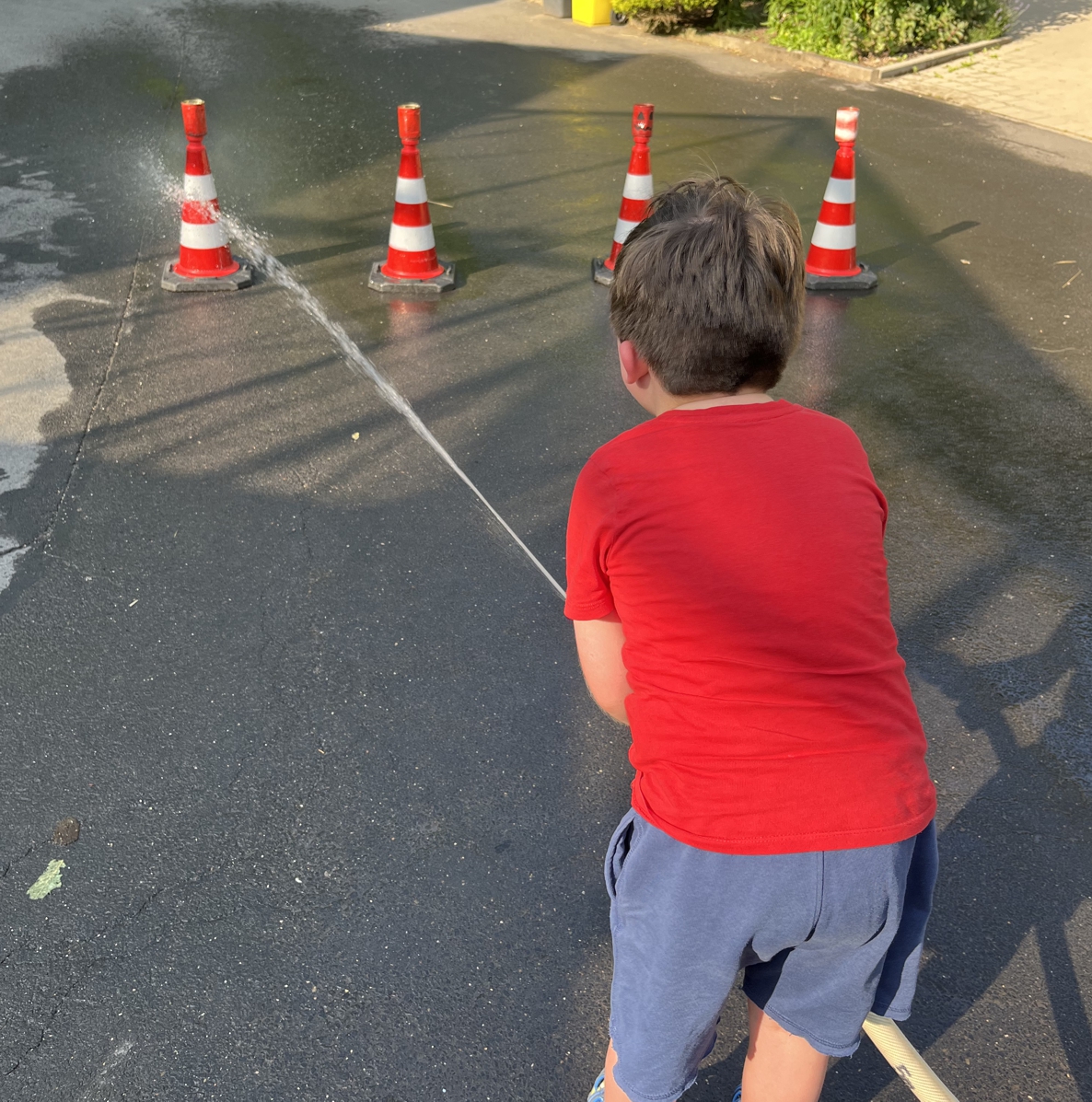 Dreamnight 2025_A.Japes (3) Ein kleiner Junge spritzt mit einem Feuerwehrschlauch Dosen von Pylonen herunter